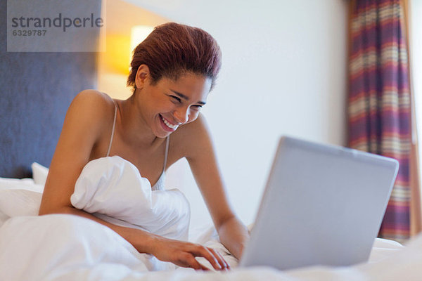 Glückliche junge Frau mit Laptop im Bett
