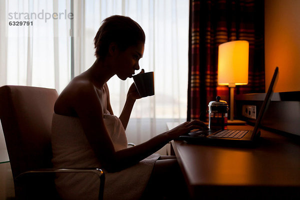 Junge Frau sitzt am Laptop im Hotelzimmer
