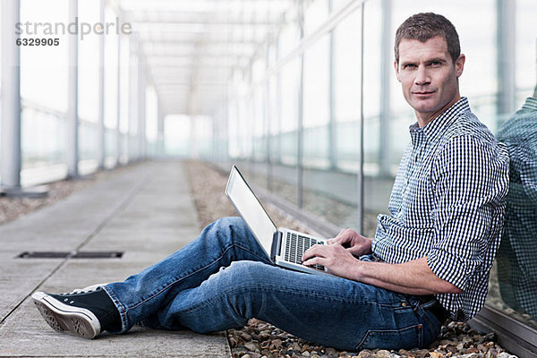 Mann auf dem Boden sitzend mit Laptop