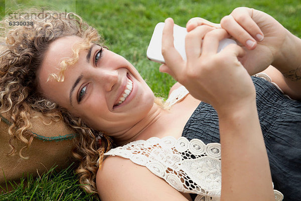 Junge Frau auf Rasen liegend mit Smartphone