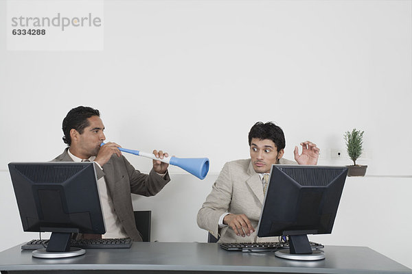 Geschäftsmann bläst Vuvuzela-Horn ins Ohr des Kollegen