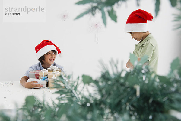 Junge hält Arm voller Weihnachtsgeschenke  lächelt schelmisch auf den launischen Bruder.