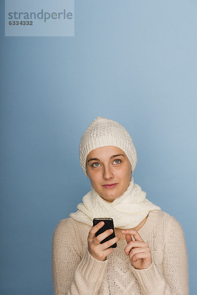 Junge Frau  die ihr Handy benutzt und in Gedanken aufschaut.