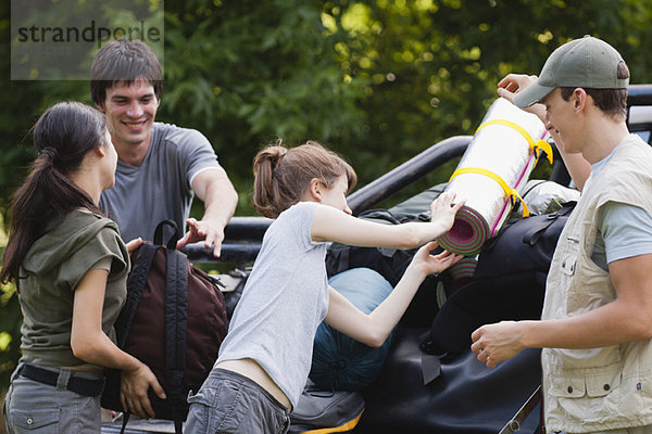 Junge Männer helfen jungen Frauen beim Verladen der Campingausrüstung auf die Ladefläche des Pick-up Trucks