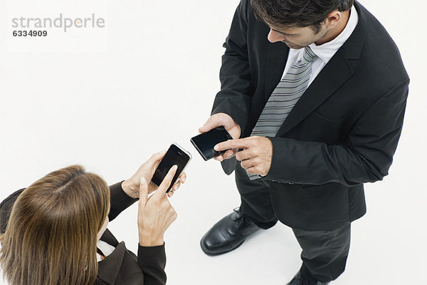 Geschäftsfrau und Geschäftsmann von Angesicht zu Angesicht  beide mit Hilfe von Smartphones