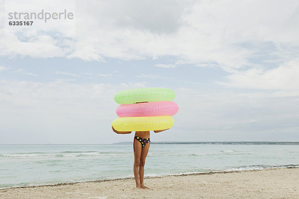 Mädchen hält Stapel von aufblasbaren Ringen am Strand  Gesicht verdeckt