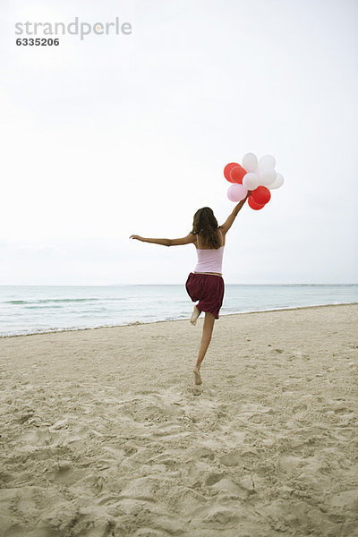 Frau läuft am Strand mit Luftballons  Rückansicht