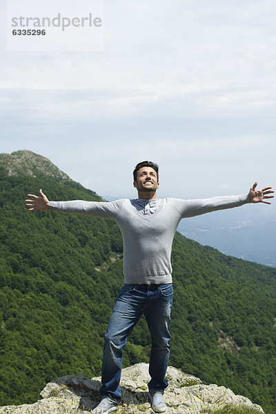 Mittelalterlicher Mann am Felsrand stehend mit ausgestreckten Armen  Berglandschaft im Hintergrund