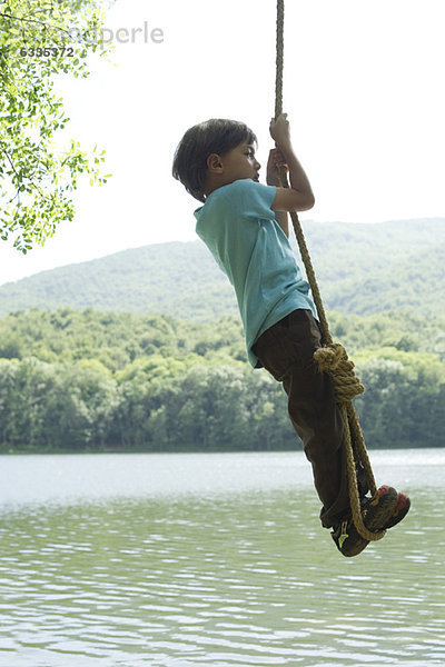 Junge hängt am Seil über dem Fluss