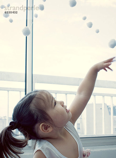 Kleines Mädchen schaut zur Pompon-Girlande hoch