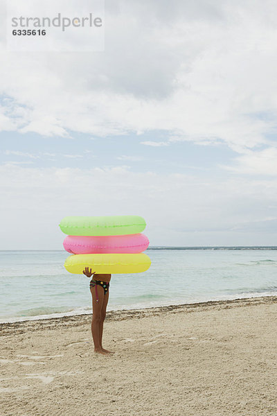 Mädchen hält Stapel von aufblasbaren Ringen am Strand  Gesicht verdeckt