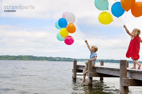 Kinder halten Luftballons auf Holzpfeiler