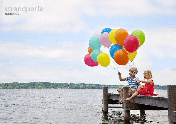 Kinder halten Luftballons auf Holzpfeiler