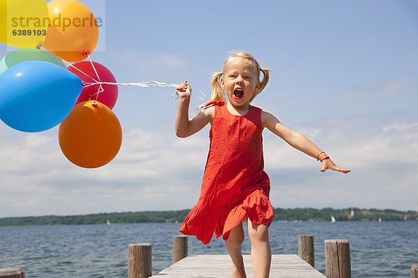 Mädchen hält Luftballons auf Holzpfeiler