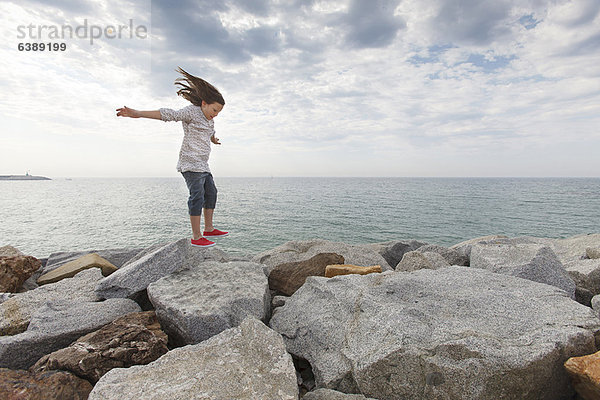 Mädchen spielt auf Felsen am Strand