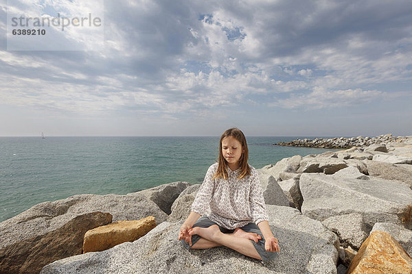 Mädchen beim Meditieren auf Felsen am Strand