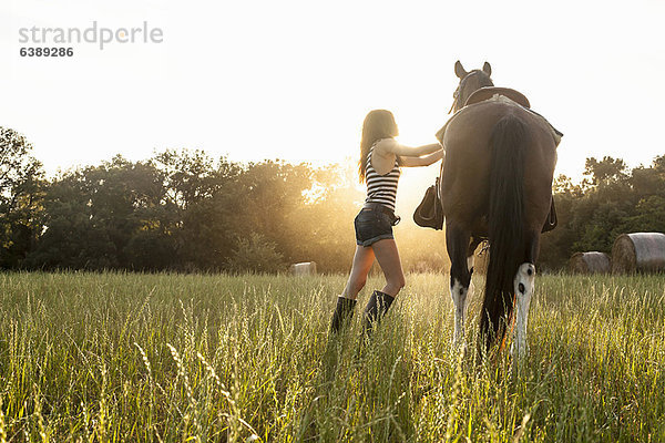 Frau sattelt Pferd im Feld auf