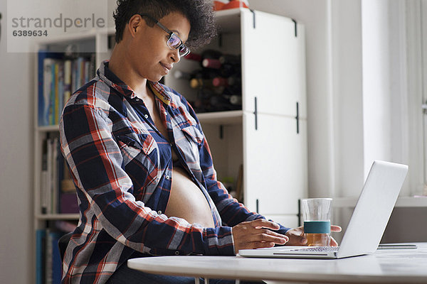 Schwangere Frau mit Laptop in der Küche