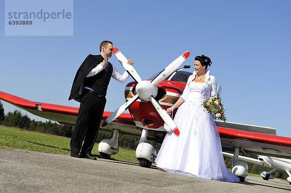 Junges Brautpaar posiert vor einem Propellerflugzeug