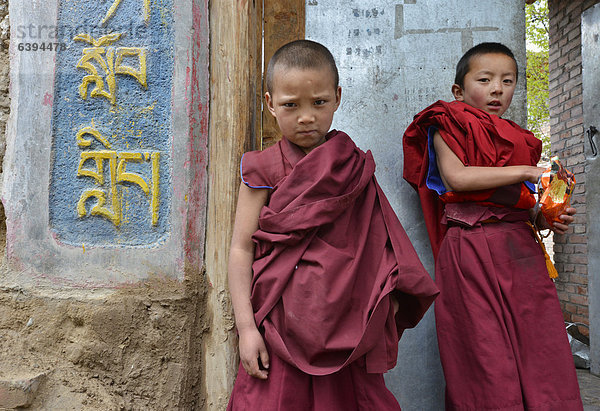 Zwei junge Novizen  Mönchsschüler vor dem Eingang zu buddhistischer Klosterschule  Klostergebäude im traditionellen Baustil  Kloster Tongren  Repkong  Qinghai  ehemals Amdo  Tibet  China  Asien