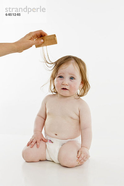 Ein kleines Mädchen  das sich die Haare kämmen lässt.