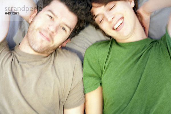 Ein junges Paar auf einem Bett nebeneinander liegend  lachend  Nahaufnahme