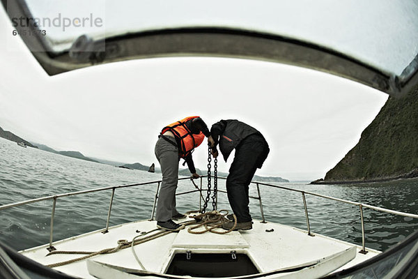 Zwei Personen  die einen Anker vom Bug eines Bootes senken  Avacha Bay  Russland