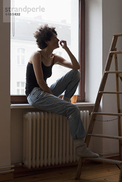 Eine Frau  die auf einem Fensterbrett sitzt und ihren Fuß auf einer Leiter ruht