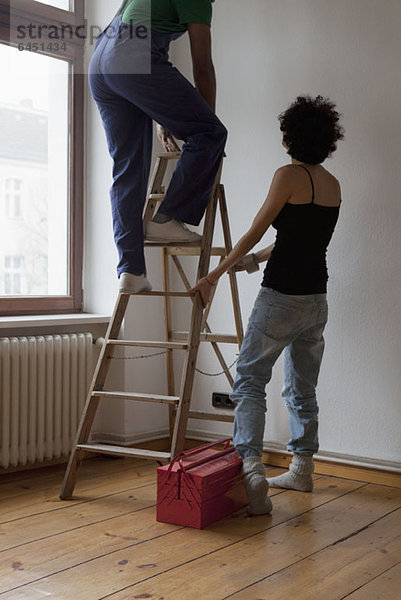Eine Frau hält eine Leiter  während ein Mann aufsteigt.