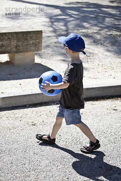 Ein kleiner Junge  der mit einem Ball läuft.