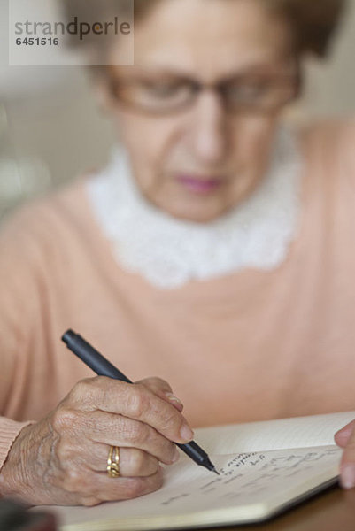 Detail einer älteren Frau beim Schreiben in einem Notizbuch
