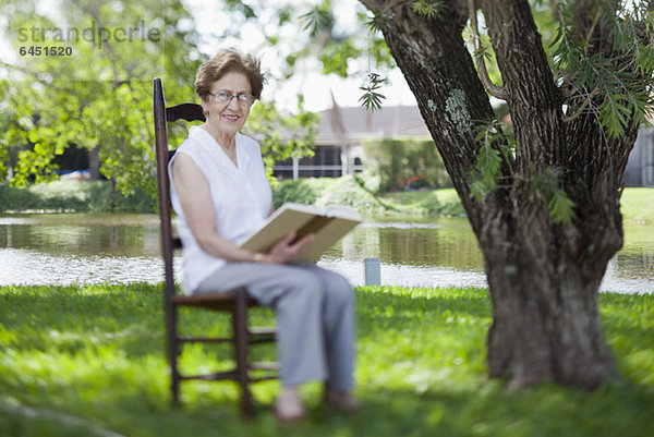 Eine ältere Frau liest am Fluss.