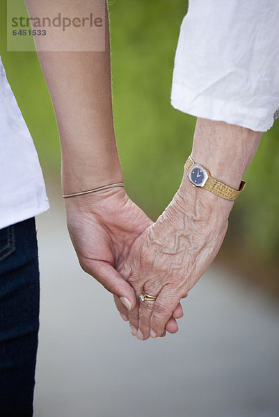 Detail einer älteren Frau und einer jungen Frau beim Händchenhalten