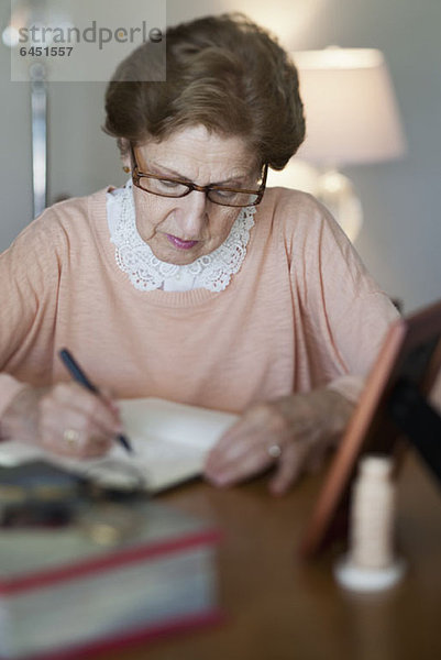 Eine ältere Frau  die in ein Notizbuch schreibt.