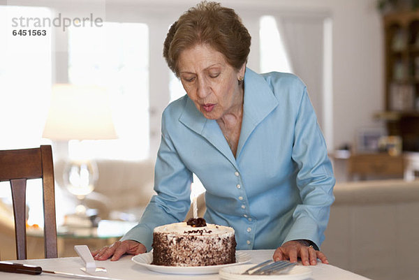 Eine ältere Frau  die eine Kerze auf einem Kuchen ausbläst.