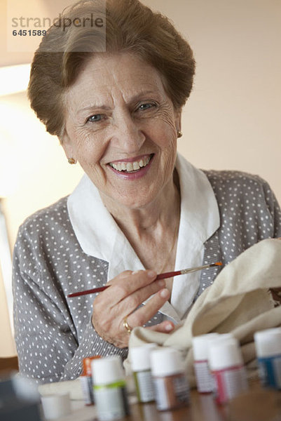 Eine ältere Frau malt auf Stoff