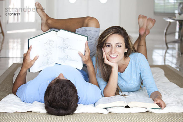 Ein junges Paar liegt auf dem Boden und lernt mit Lehrbüchern.