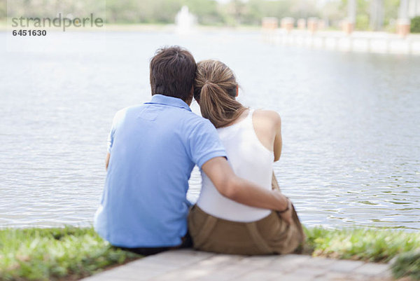 Ein liebevolles Paar sitzt am See  Rückansicht