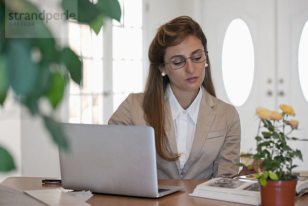 Eine Geschäftsfrau  die einen Laptop benutzt und ein Buch an ihrem Schreibtisch liest.