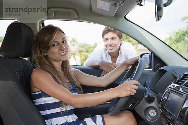 Ein Mann  der im Autofenster lehnt und die Freundin auf dem Fahrersitz anlächelt.