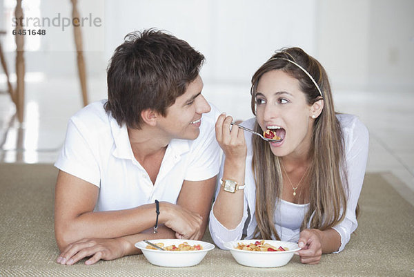 Ein junges Paar liegt auf dem Boden und isst Müsli zum Frühstück.