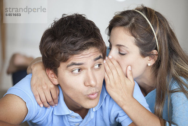 Ein Mann  der überrascht sieht  was seine Freundin ihm ins Ohr flüstert.