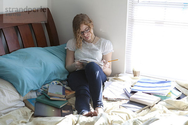 Beschäftigtes Mädchen mit Studienbüchern auf dem Bett
