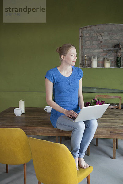 Eine Frau  die mit einem Laptop auf ihrem Esstisch sitzt.