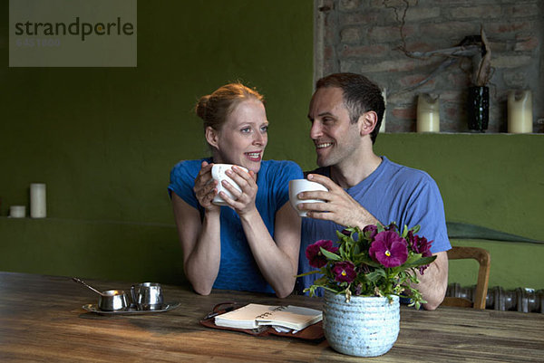 Ein Paar sitzt am Esstisch mit einem Terminplaner und spricht bei einem Kaffee.