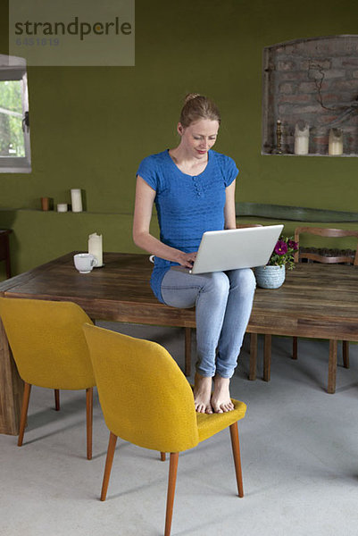 Eine Frau  die mit einem Laptop auf ihrem Esstisch sitzt.