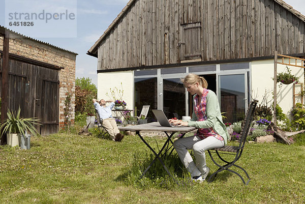 Eine Frau  die einen Laptop benutzt und in ihrem Garten frühstückt.