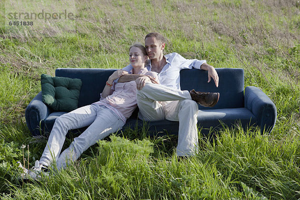 Ein Paar  das auf einem Sofa in einem Grasfeld sitzt.