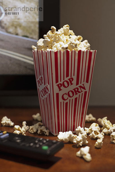 Ein rot gestreifter Karton Popcorn auf einem Tisch vor einem Flachbildfernseher