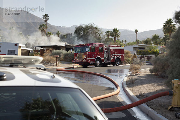 Ein Polizeiauto und ein Feuerwehrauto am Tatort eines brennenden Hauses in einem Vorort